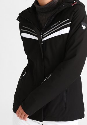 Zwarte jas met ritssluiting, witte en grijze strepen over de borst, een capuchon en ritssluitingen aan de zijkanten, gedragen over een donkere coltrui.