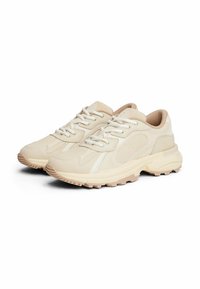 Baskets de sport beiges avec une tige texturée, ornées d'accents blancs, de semelles en caoutchouc épaisses et de lacets pour un ajustement sécurisé.