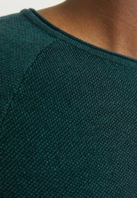 Mörk teal stickad tröja med en strukturerad yta, med en ribbad halsringning och raglanärmar. Mjuk tygkvalitet med en åtsittande passform.