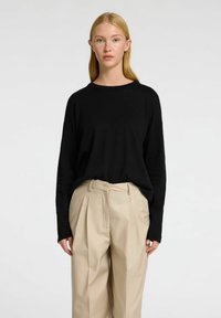 Černý svetr s dlouhým rukávem a kulatým výstřihem, doplněný o světle béžové kalhoty s vysokým pasem, které mají sklady a upravený střih.