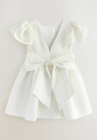 Witte jurk met korte, bolvormige mouwen versierd met kleine parels. Heeft een diepe V-rug en een grote strik aan de voorkant, gezekerd met een parelaccent.