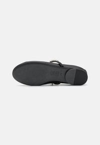 Sandal noir avec un dessus en cuir lisse, semelle plate et bout rond. Présente un accent en perle sur la sangle. Fond en caoutchouc texturé pour une meilleure adhérence.