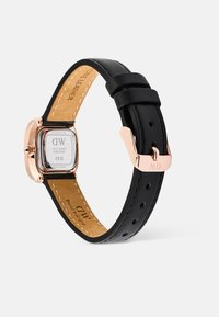 Montre avec bracelet en cuir noir et boîtier en acier rose doré carré, dotée d'un cadran blanc et d'une fermeture à boucle ardillon. L'arrière affiche des informations sur la marque.