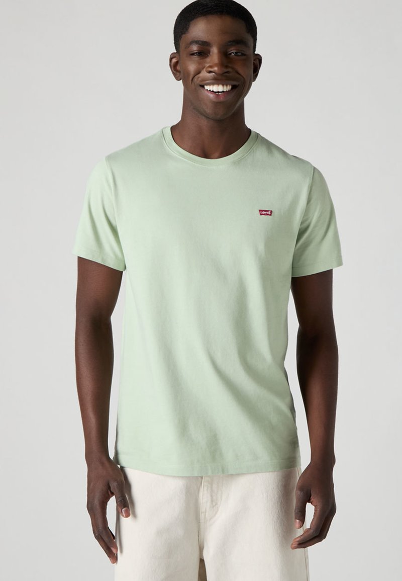 T-shirt en coton vert clair avec un col rond, des manches courtes et un petit logo rouge Levi's sur la poitrine. Coupe simple et classique sans motifs.