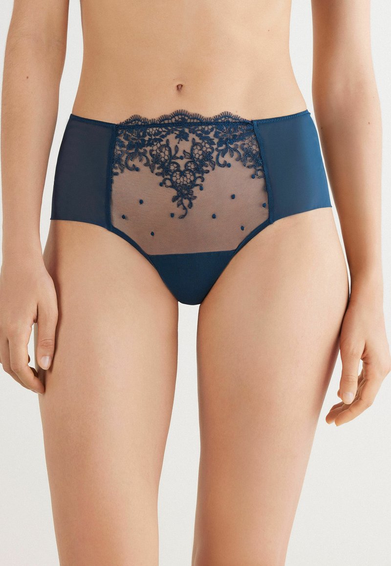 Navyblauwe high-waisted onderbroeken met doorschijnende meshpanelen, ingewikkelde kantdetails en kleine versierde stippen aan de voorkant.