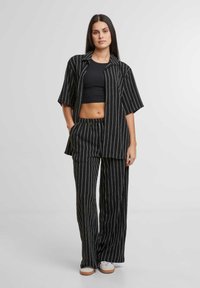 Completo a righe nere composto da una camicia a maniche corte con chiusura a bottoni, pantaloni larghi con cintura elastica e sneakers bianche.
