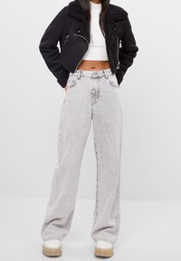 Svart kort jacka med fårskinnskrage, matchad med högmidjade ljusgrå vida jeans och beiga platåskor.