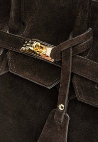 Zamszowa torebka w ciemnym brązie o gładkiej fakturze. Posiada złoty metalowy zamek oraz ozdobny pasek z detalem w postaci ćwieka.