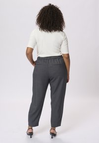 Pantaloni grigi su misura con vestibilità comoda e vita elasticizzata, abbinati a un top crema aderente. Il tessuto è liscio e presenta tasche posteriori discrete.