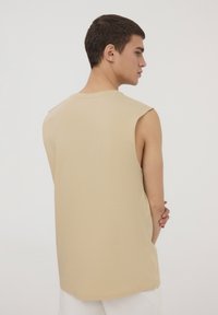 Top in cotone beige senza maniche con scollatura rotonda e vestibilità rilassata. Presenta armholes leggermente scesi e orlo dritto.