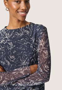 Bluză bleumarin cu mâneci lungi transparente, decorată cu un model abstract alb în spirală. Decolteu rotund și țesătură texturată, cu o croială lejeră.
