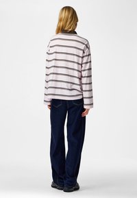 Långärmad t-shirt med rosa och vita ränder och en brun krage, kombinerad med mörkblå, löst sittande jeans och svarta skor.