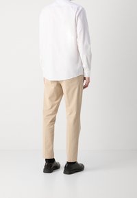 Camicia bianca a maniche lunghe con polsini con bottoni, abbinata a pantaloni beige e scarpe nere. Caratterizzata da un taglio dritto e un design minimale.