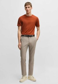 T-shirt a maniche corte color ruggine, pantaloni beige su misura, cintura marrone e sneakers color crema, caratterizzati da superfici lisce e un design aderente.