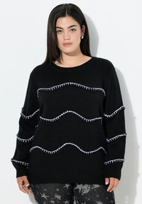 Schwarzer Strickpullover mit Rundhalsausschnitt und weißen Zickzackn�ähten. Lange Ärmel und bequeme Passform, kombiniert mit Hosen im Sternenmuster.