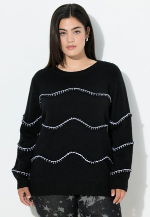 Sort strikket sweater med rund hals og hvid zigzag-syning. Langærmede og med en afslappet pasform, parret med bukser med stjernemønster.
