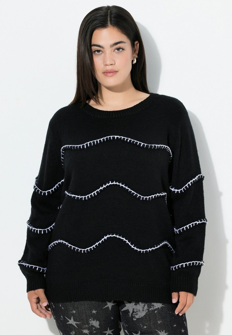 Schwarzer Strickpullover mit Rundhalsausschnitt und weißen Zickzacknähten. Lange Ärmel und bequeme Passform, kombiniert mit Hosen im Sternenmuster.