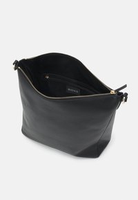 Sac à main en cuir noir avec fermeture éclair dorée partiellement ouverte, montrant une poche intérieure zippée étiquetée "BOSS" sur un fond clair uni.