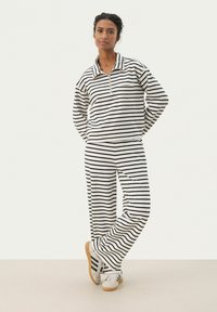 Ribade loungewear komplekt valge ja musta värviga, sisaldades tõmblukuga kõrge kaelusega särki ja laia jalgadega pükse. Pehme kangas, millel on lõdvestunud sobivus. Kaunistatud rinna taskuga.