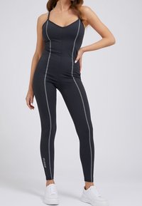 Combinaison de sport noire avec des rayures verticales grises, bretelles fines et un design ajusté. Associée à des baskets blanches pour le contraste.