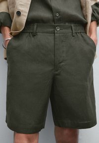 Dark green linen shorts featuring a button closure, elastic waistband, two side pockets, and a relaxed fit.