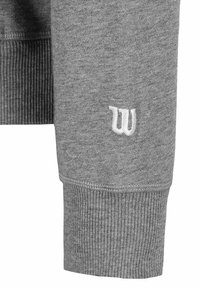 Grauer Sweatshirtärmeln mit elastischem Rippbündchen. Verfügt über ein kleines, weiß gesticktes Logo in der Nähe des Bündchens. Hergestellt aus weichem Stoff.