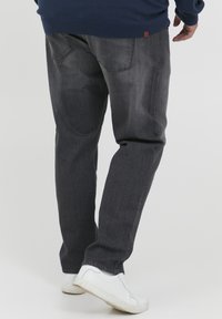 Dark gray jeans made of denim, featuring a straight leg cut, two back pockets, and subtle contrast stitching, paired with white sneakers.