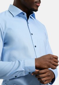 Himmelblaues Hemd mit Knöpfen, mit einem strukturierten Muster, langen Ärmeln und dunkelblauen Knöpfen. Verfügt über einen klassischen Kragen und geknöpfte Manschetten.