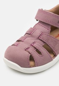 Pink suede sandal with multiple cutouts, adjustable strap, white rubber sole, and contrasting pink stitching details.