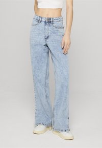 Gaiši zilas, augsti jostasvietas džinsa bikses ar vaļēju piegriezumu, ar pogu aizdari, piecām kabatām un nelielām svītru detaļām priekšpusē.