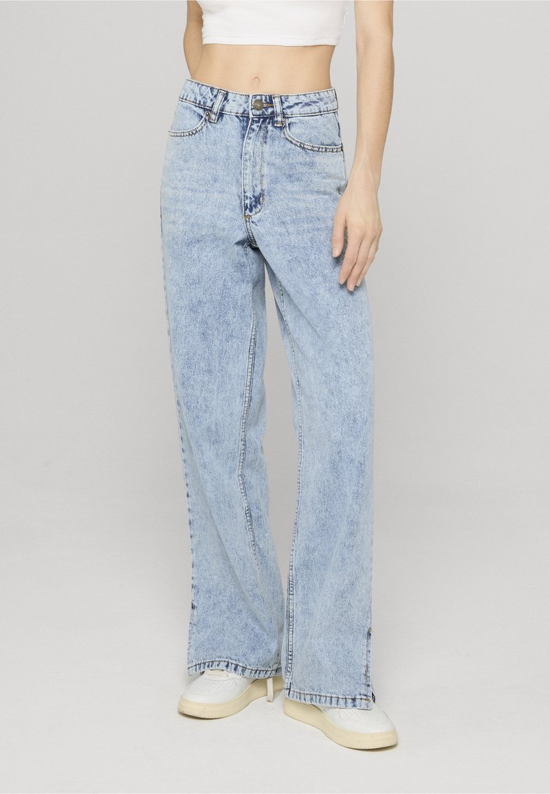 Gaiši zilas, augsti jostasvietas džinsa bikses ar vaļēju piegriezumu, ar pogu aizdari, piecām kabatām un nelielām svītru detaļām priekšpusē.