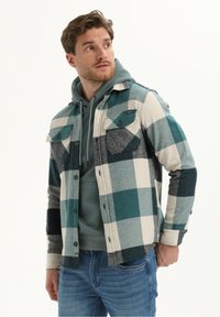 Geruit flanellen shirt in teal, grijs en room, met twee borstzakken, knopen aan de voorkant en een ontspannen pasvorm over een grijze hoodie.
