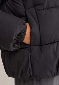 Melnā pūkaino jakā ar quilted dizainu un elastīgiem rokas galiem. Iespējas sānu kabatai ar gludu, matētu apdari. Mīksts, viegls materiāls.