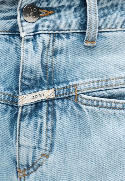 Ανοιχτό μπλε τζιν με μεταλλικό κουμπί και μικρή ετικέτα, και τα δύο χαραγμένα με το όνομα της μάρκας «CLOSED».