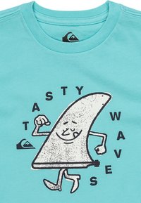 Camiseta de algodón turquesa con un personaje de dibujos animados con forma triangular, brazos y texto que dice "TASTY WAVE". Diseño gráfico simple.