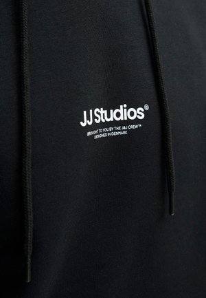 Zwarte hoodie van zacht materiaal, met een wit logo "JJ Studios" op de borst en zwarte koorden met metalen punten.