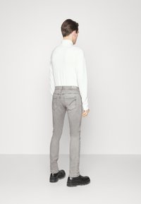 Grå denimjeans med slim fit, femfickorsdesign och kontrasterande sömmar. Bärs med en vit långärmad topp och svarta stövlar.