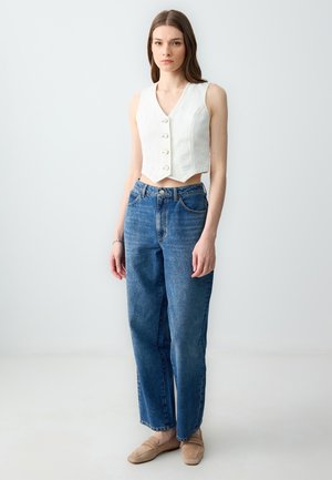 Top bianco cropped con bottoni, abbinato a jeans blu a vita alta. Texture morbida, design a gamba dritta e denim lavato chiaro.