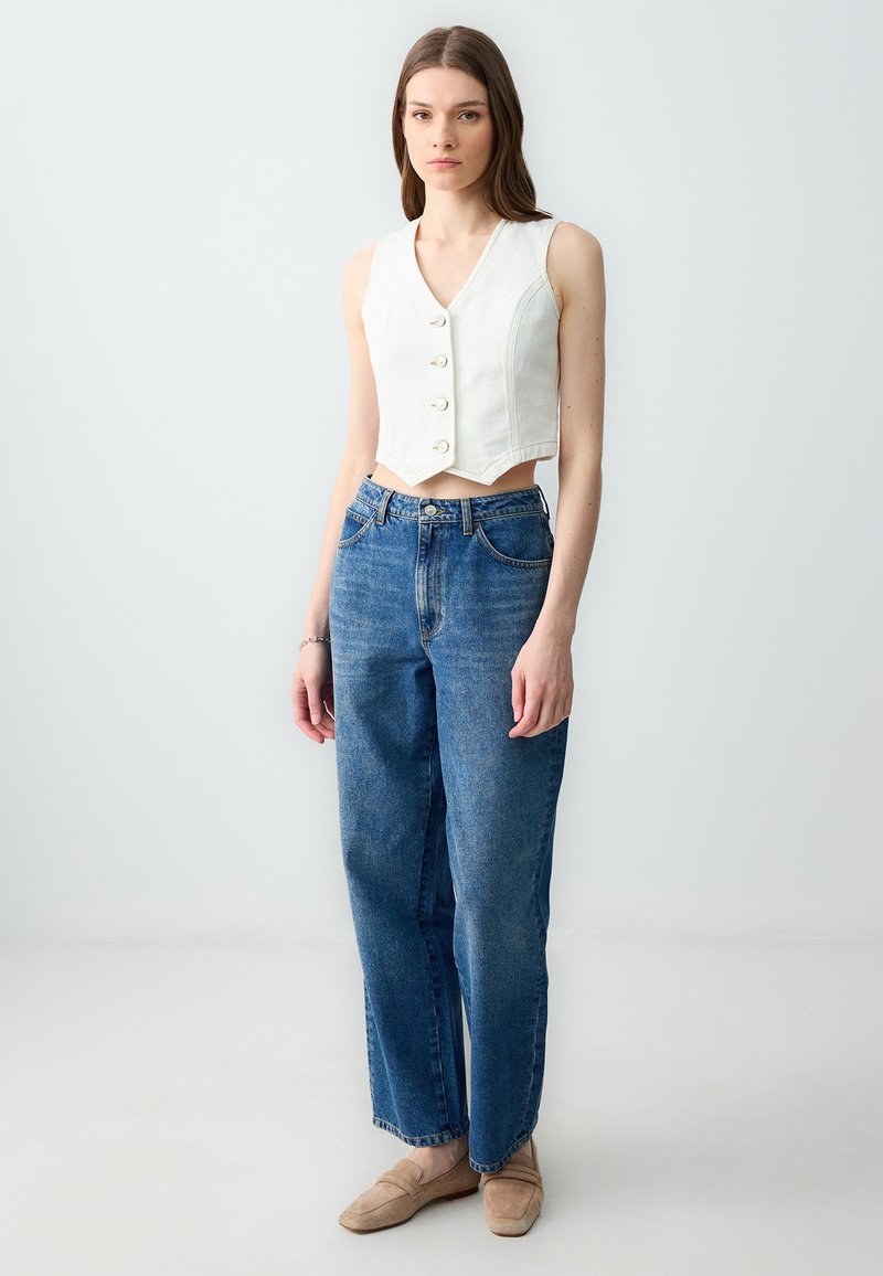 Top bianco cropped con bottoni, abbinato a jeans blu a vita alta. Texture morbida, design a gamba dritta e denim lavato chiaro.
