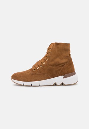 Bottines en daim marron avec œillets dorés, semelle intermédiaire blanche et semelle texturée. Caractérisées par un bout arrondi et des coutures apparentes.