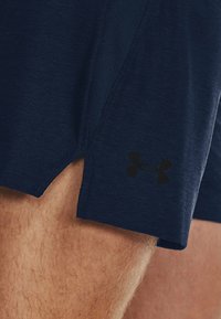 Shorts deportivos color azul marino con un corte lateral, fabricados con un tejido texturizado. Presentan un logo negro de Under Armour en el dobladillo inferior.