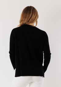 Maglione nero a maglia con maniche lunghe, polsini e orlo a costine. Morbido al tatto con una vestibilità rilassata. Vista posteriore che mostra un design semplice.