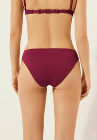 Burgundy bikiniunderdel med en texturerad mönster. Midjehöjd, slät midjeband och en klippning som erbjuder måttlig täckning bak.