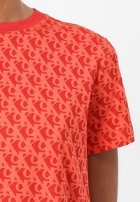 Red short-sleeve t-shirt featuring a textured all-over wave pattern, crew neck, and contrasting collar with a smooth fabric finish.
