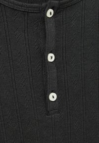 Crni rebrasti top s okruglim izrezom, vertikalnom teksturom i tri bijele gumbe uz prednji otvor.