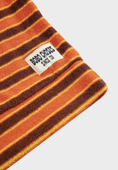 Tela a rayas naranjas, marrones y amarillas con una etiqueta rectangular blanca cosida que dice "BOBO CHOSES SINCE '09".