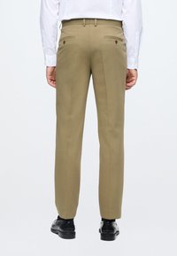 Beige Anzughosen mit geradem Bein, zwei Gesäßtaschen und subtiler Textur. Verfügt über einen sauberen Bund und wird mit schwarzen Schuhen getragen.