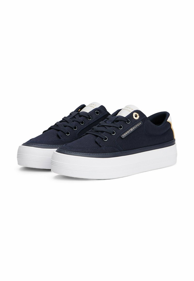 Baskets en toile navy avec semelle en caoutchouc blanc, dotées d'œillets en métal, d'un laçage et d'un patch logo sur le côté.