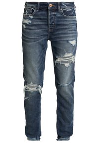 Jean en denim bleu foncé avec des déchirures usées et des ourlets effilochés ; conception à cinq poches ; fermeture à bouton en métal ; forme de jambe fuselée.