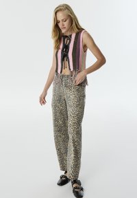Gilet all'uncinetto con strisce rosa, nere e verdi, con frange. Abbinato a pantaloni beige con stampa leopardata e scarpe nere con cinturini.